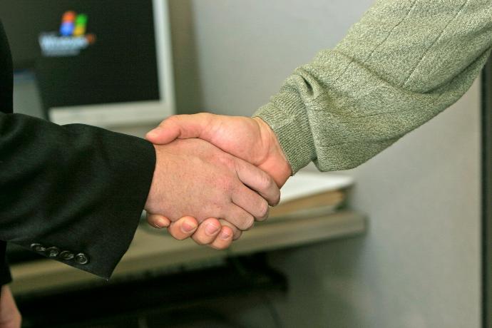 two people shaking hands in front of a computer monitor