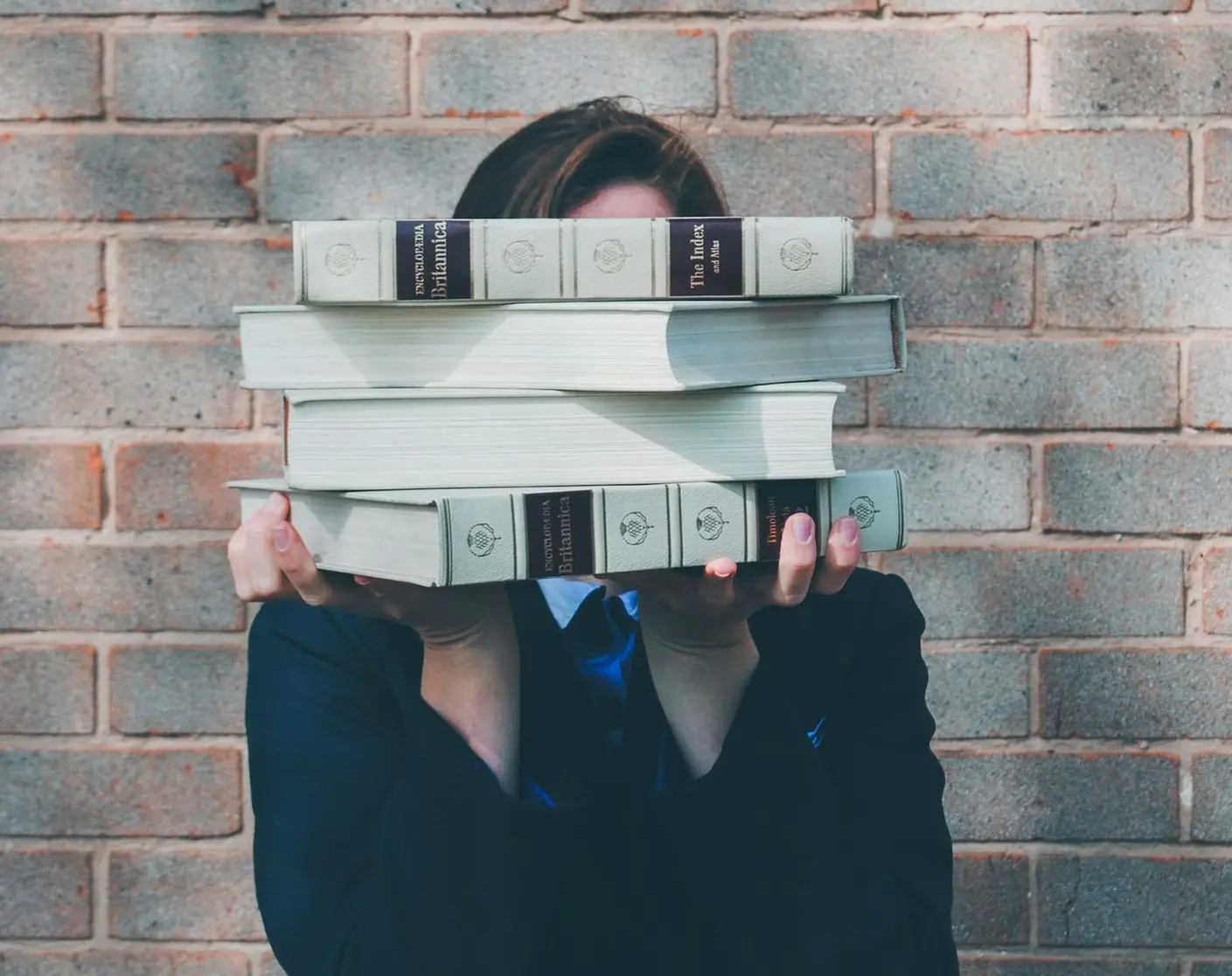 person holding pile of books near face